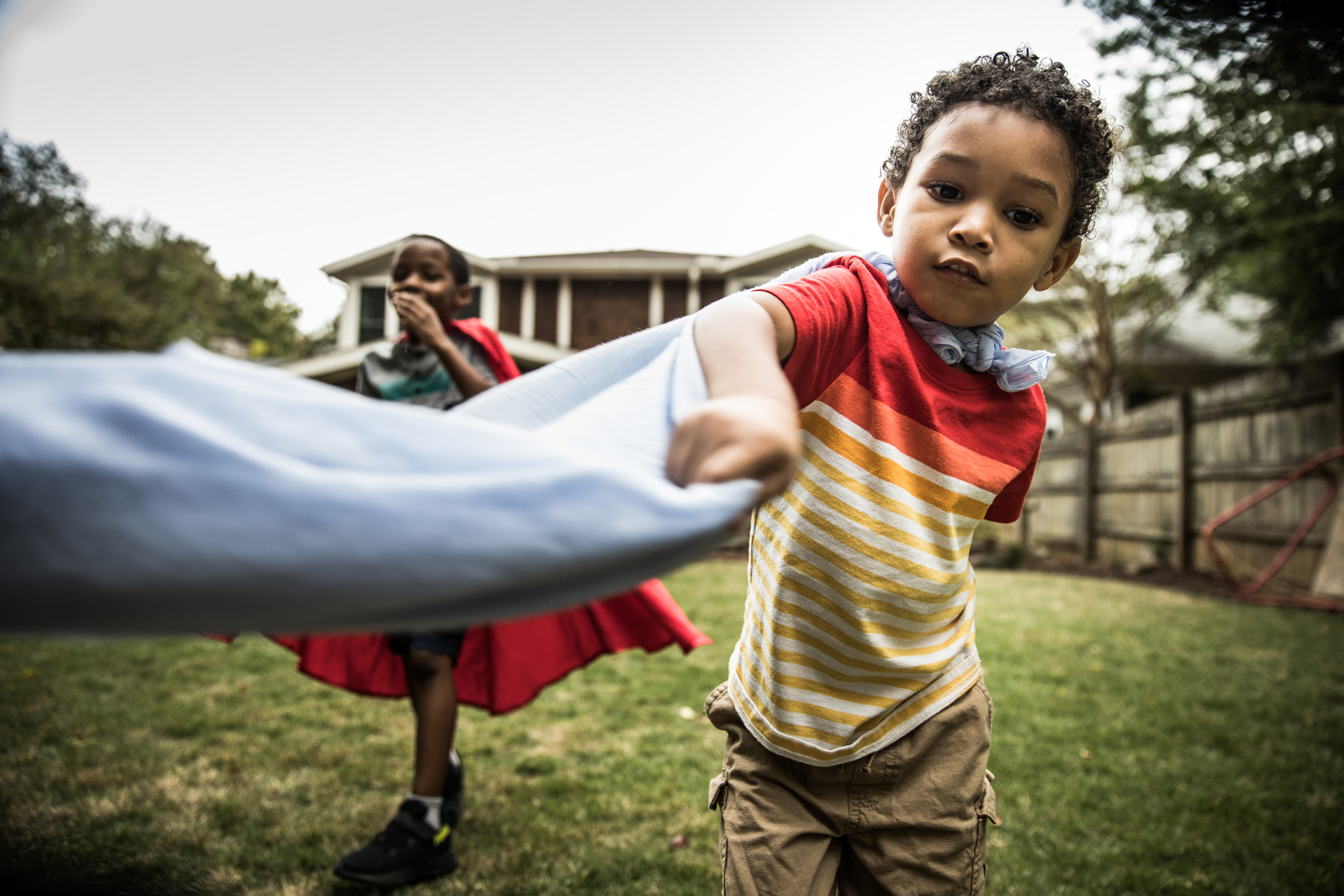 young kids running through yard in capes